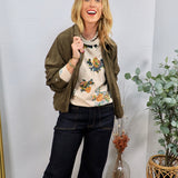 Olive green suede zip-up jacket with ruched sleeves, styled over a floral sweater and dark wide-leg jeans.