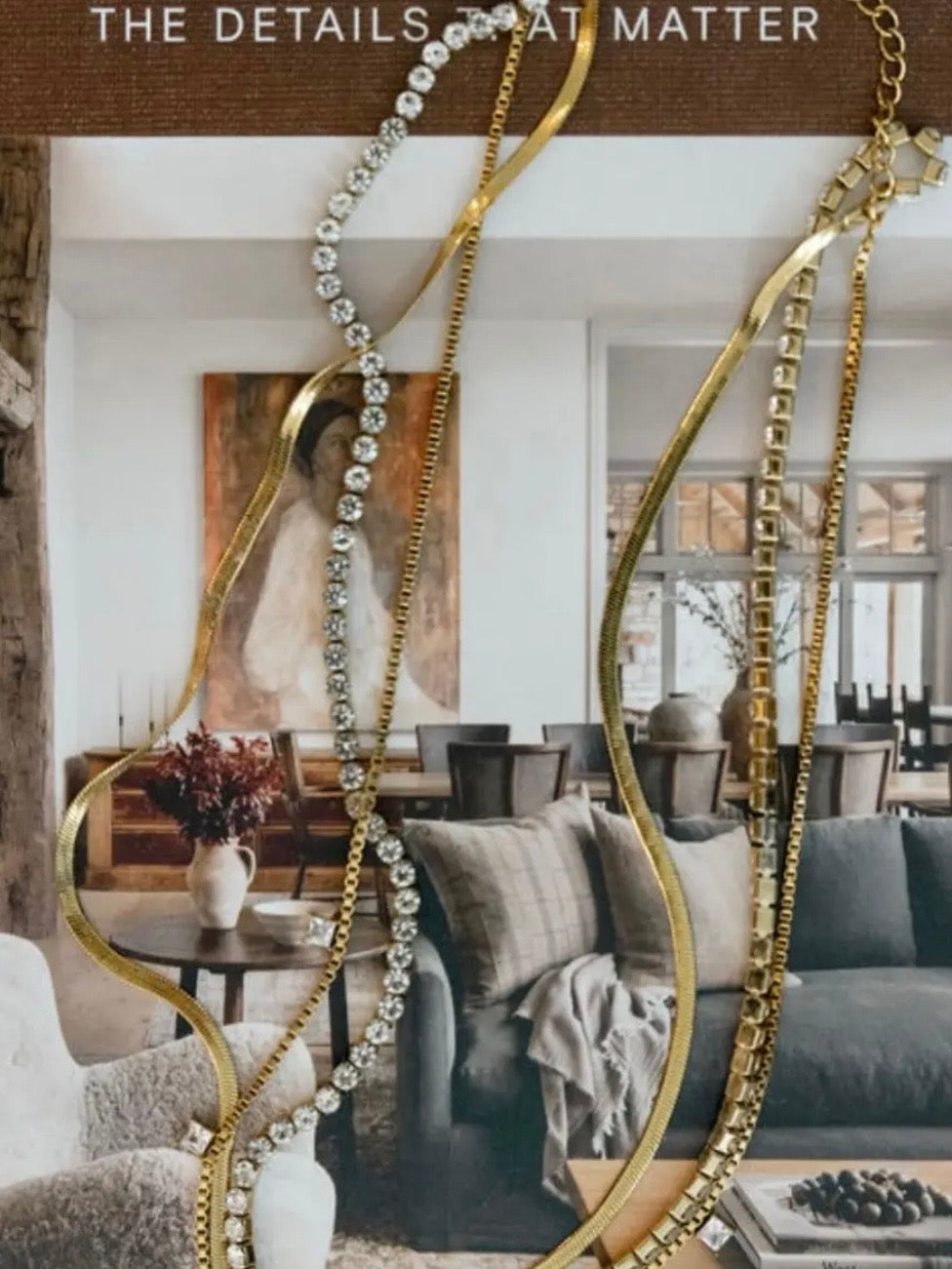 Gold herringbone, box chain, diamond tennis, and crystal necklaces draped elegantly against a neutral interior backdrop.