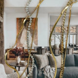 Gold herringbone, box chain, diamond tennis, and crystal necklaces draped elegantly against a neutral interior backdrop.