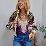 Cream zip-up knit sweater with purple and black geometric pattern, styled over purple satin cami and blue jeans.