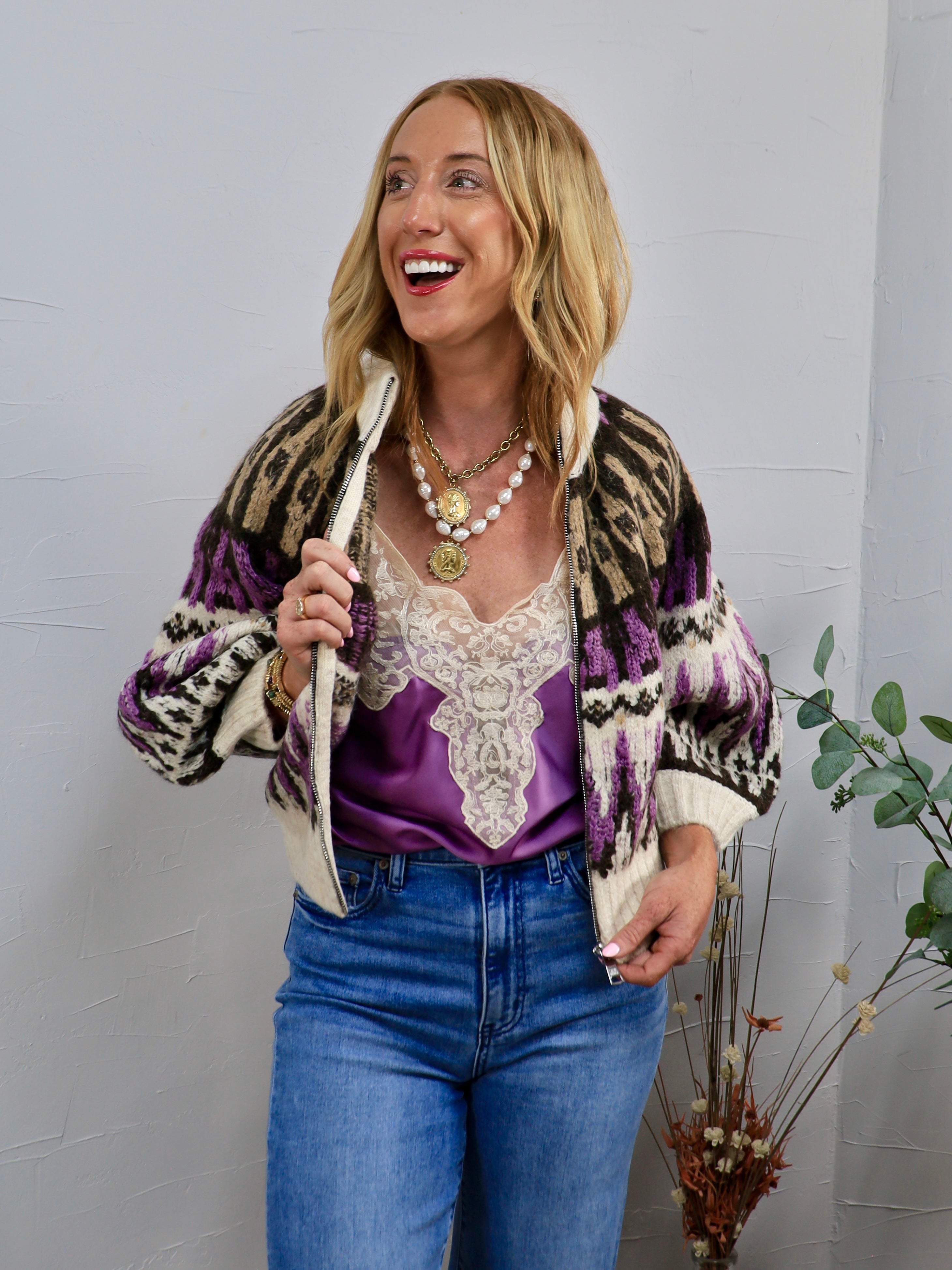 Cream zip-up knit sweater with purple and black geometric pattern, styled over purple satin cami and blue jeans.