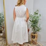 White sleeveless midi shirt dress with smocked waist, collar neckline, and flared skirt, shown from behind.