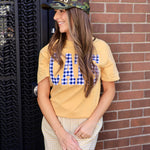 Camouflage trucker hat with gold "CHAMPS" text, styled with yellow graphic tee and plaid shorts.