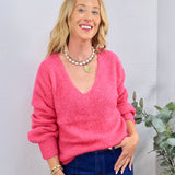 Hot pink V-neck knit sweater styled with blue jeans, pearl chain necklace, and gold coin pendant.