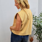 Woman wearing yellow sleeveless muscle tee with blue denim shorts, shown from behind in casual styling setup.
