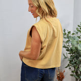 Woman wearing yellow sleeveless muscle tee with blue denim shorts, shown from behind in casual styling setup.