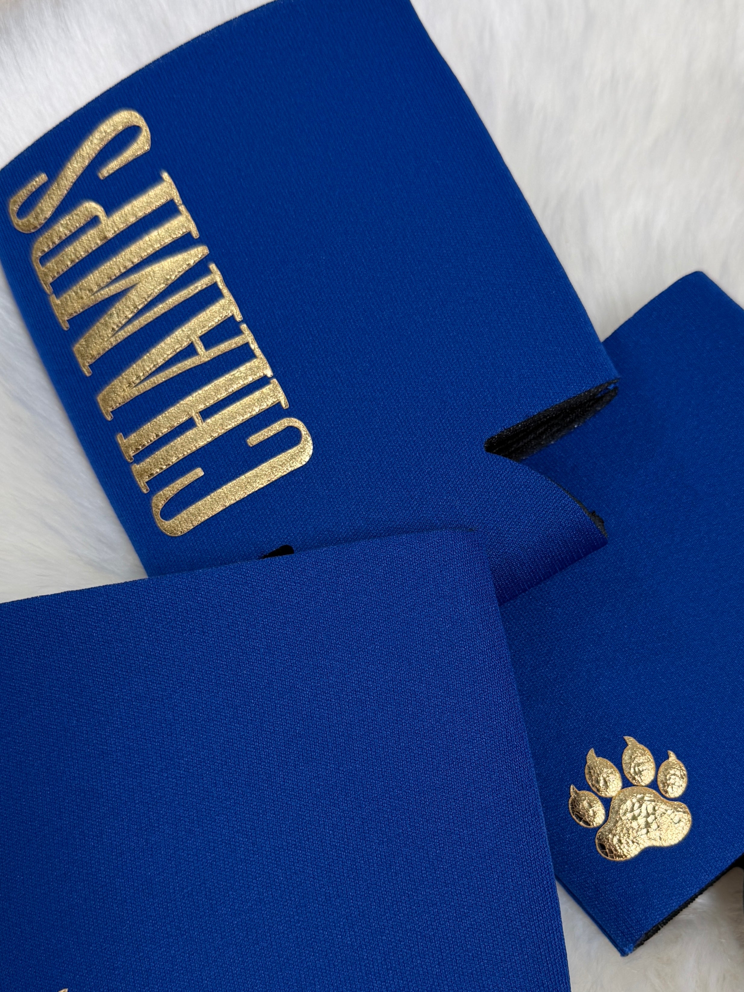Royal blue neoprene drink koozies with gold "Champs" text and gold paw print logo detail.