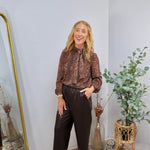 Brown floral paisley print blouse with bow tie neck and balloon sleeves, styled with dark brown faux leather pants.
