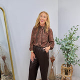 Brown floral paisley print blouse with bow tie neck and balloon sleeves, styled with dark brown faux leather pants.