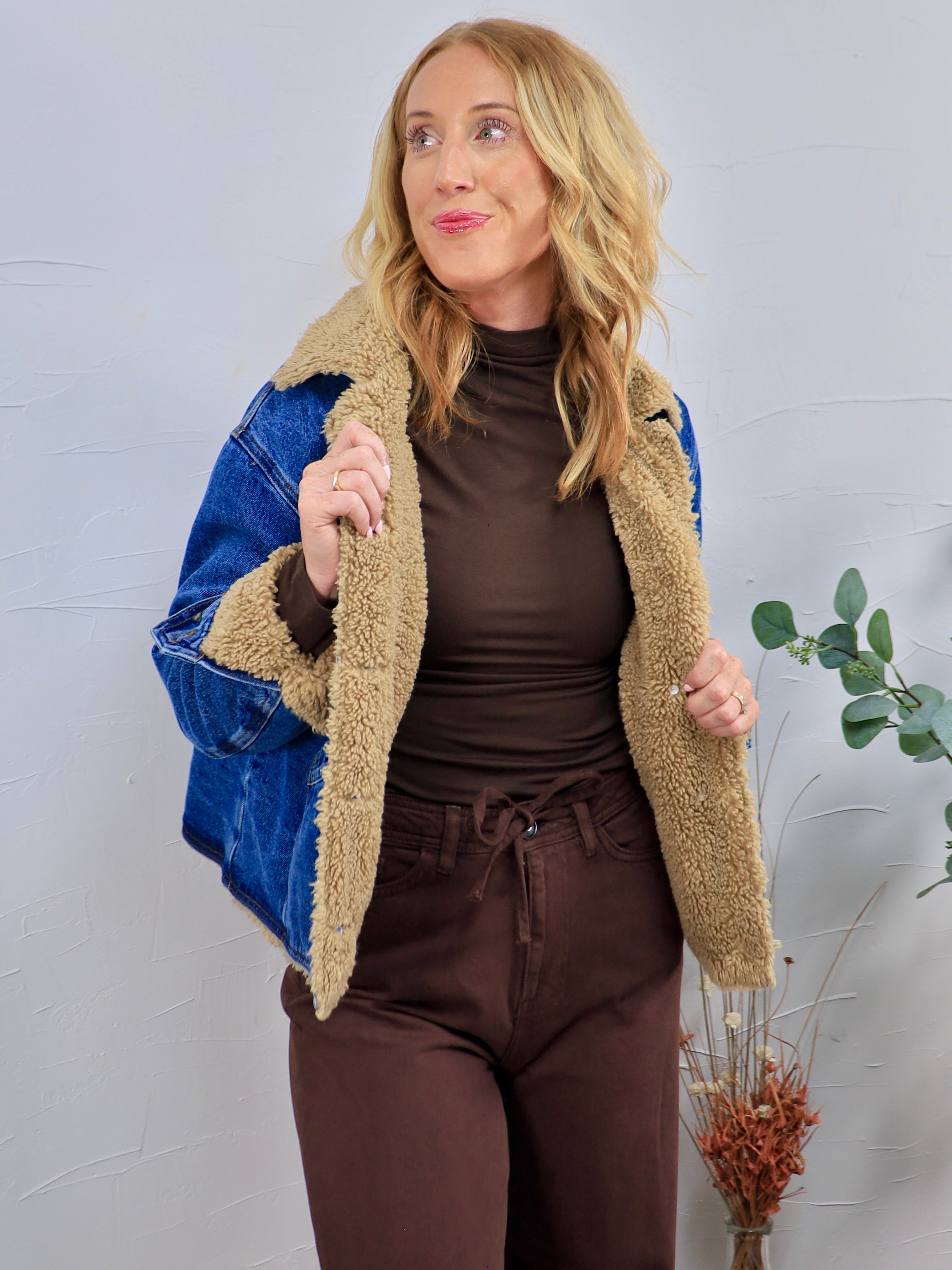 Blue denim jacket with tan sherpa teddy lining, worn open over brown turtleneck and matching brown pants.