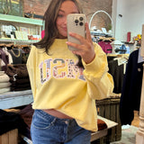 Woman wearing a soft yellow MSU patchwork appliqué crewneck sweatshirt with blue jeans
