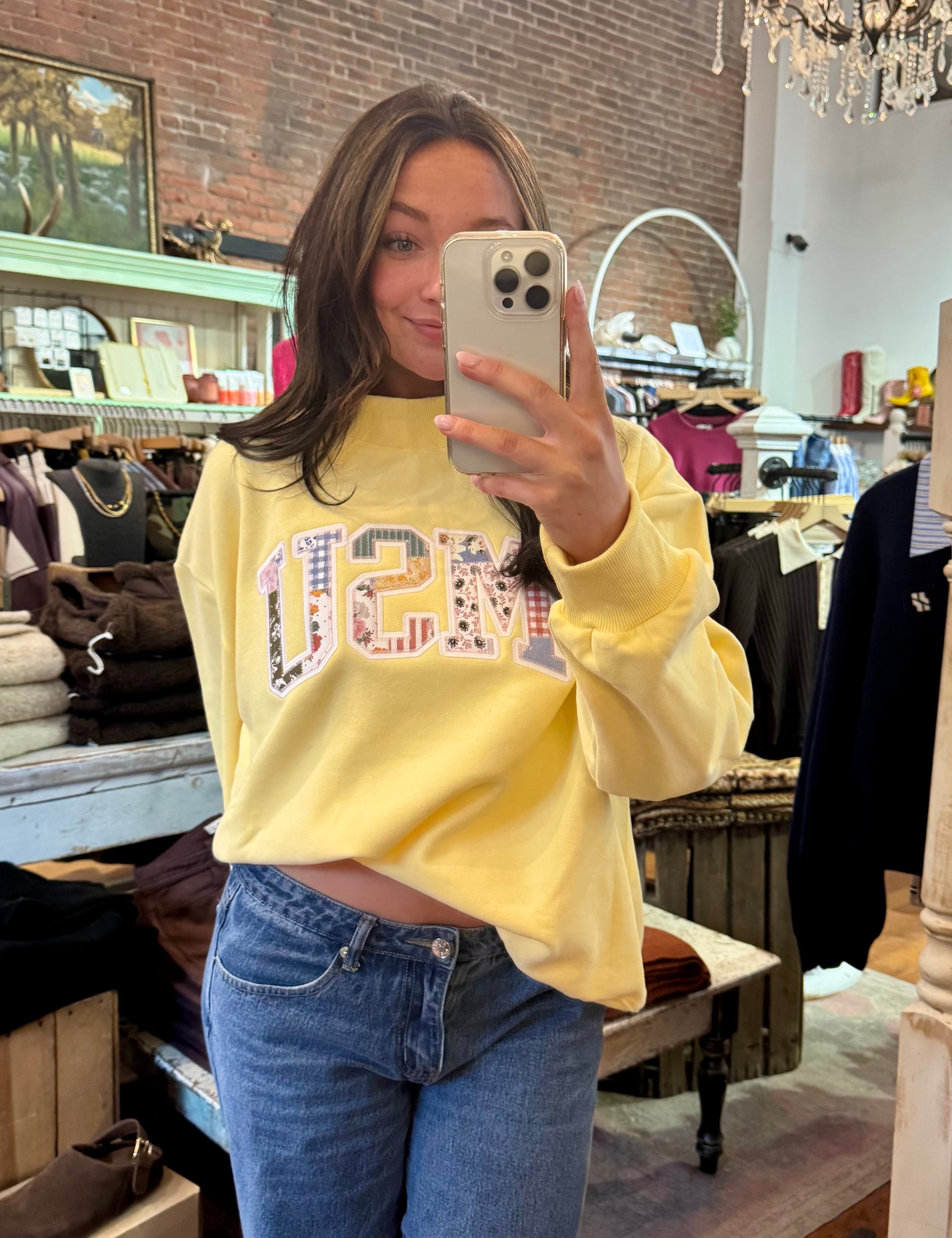 Woman wearing a soft yellow MSU patchwork appliqué crewneck sweatshirt with blue jeans