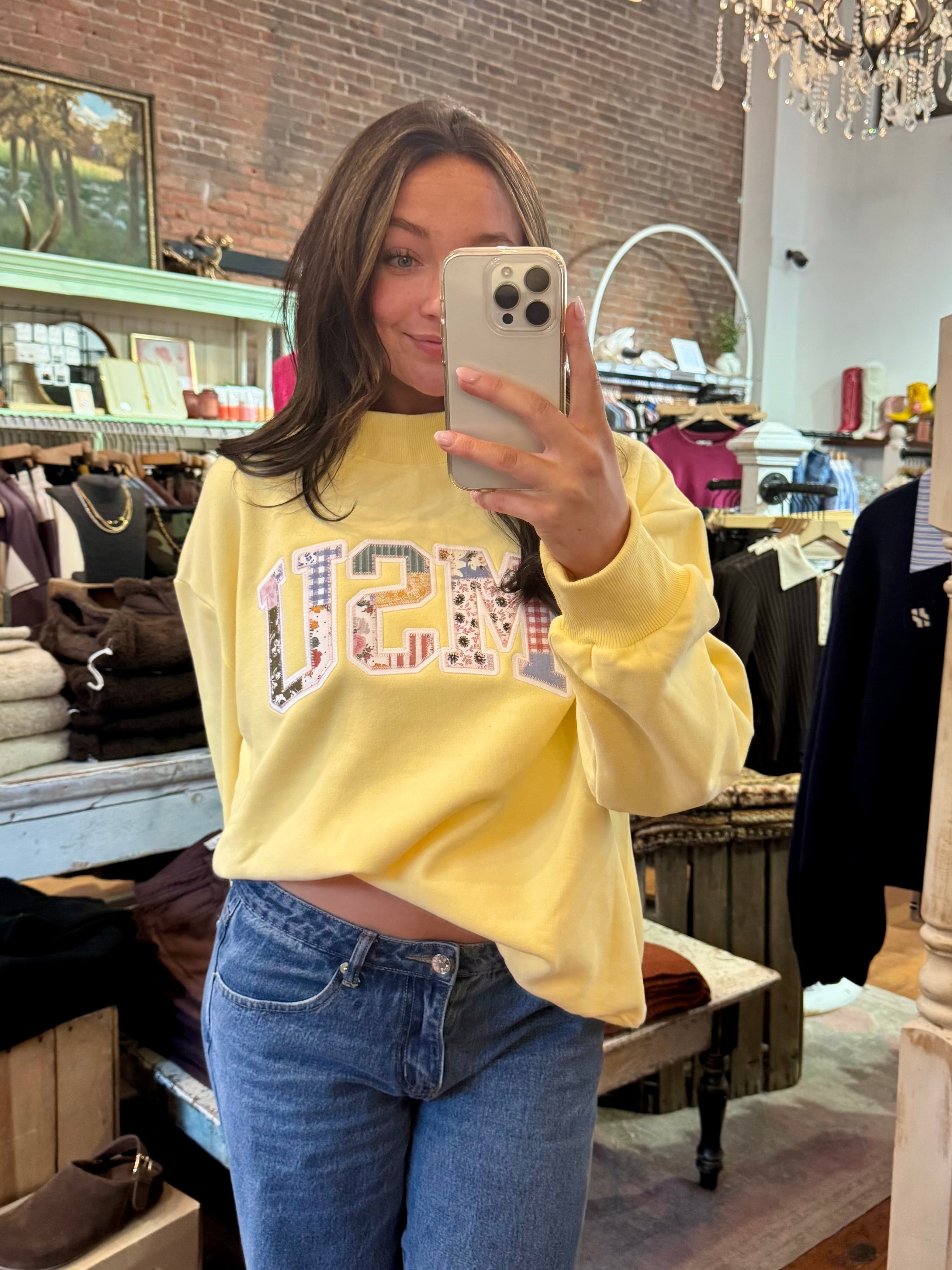 Woman wearing a soft yellow MSU patchwork appliqué crewneck sweatshirt with blue jeans