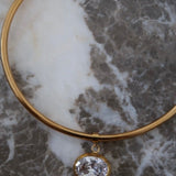 Gold rigid choker necklace with oval crystal pendant displayed on white and grey marble surface.