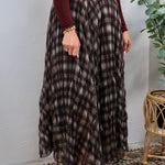 Woman wearing a dark brown plaid pleated maxi skirt with a burgundy long-sleeve top and gold bracelet