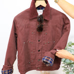 Burgundy twill bomber jacket with plaid flannel lining, corduroy collar, silver snap buttons, displayed on hanger with sungla