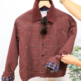 Burgundy twill bomber jacket with plaid flannel lining, corduroy collar, silver snap buttons, displayed on hanger with sungla