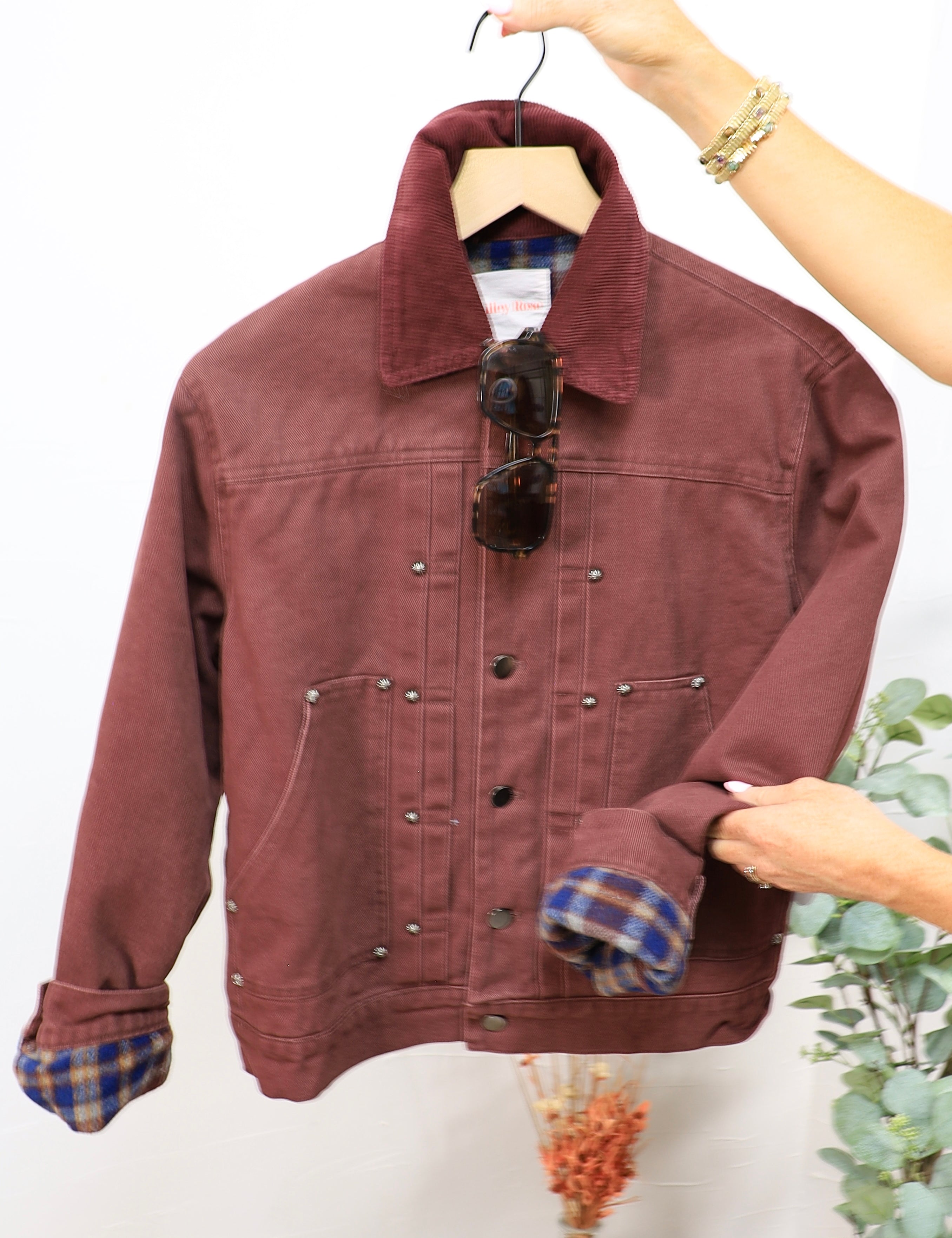 Burgundy twill bomber jacket with plaid flannel lining, corduroy collar, silver snap buttons, displayed on hanger with sungla