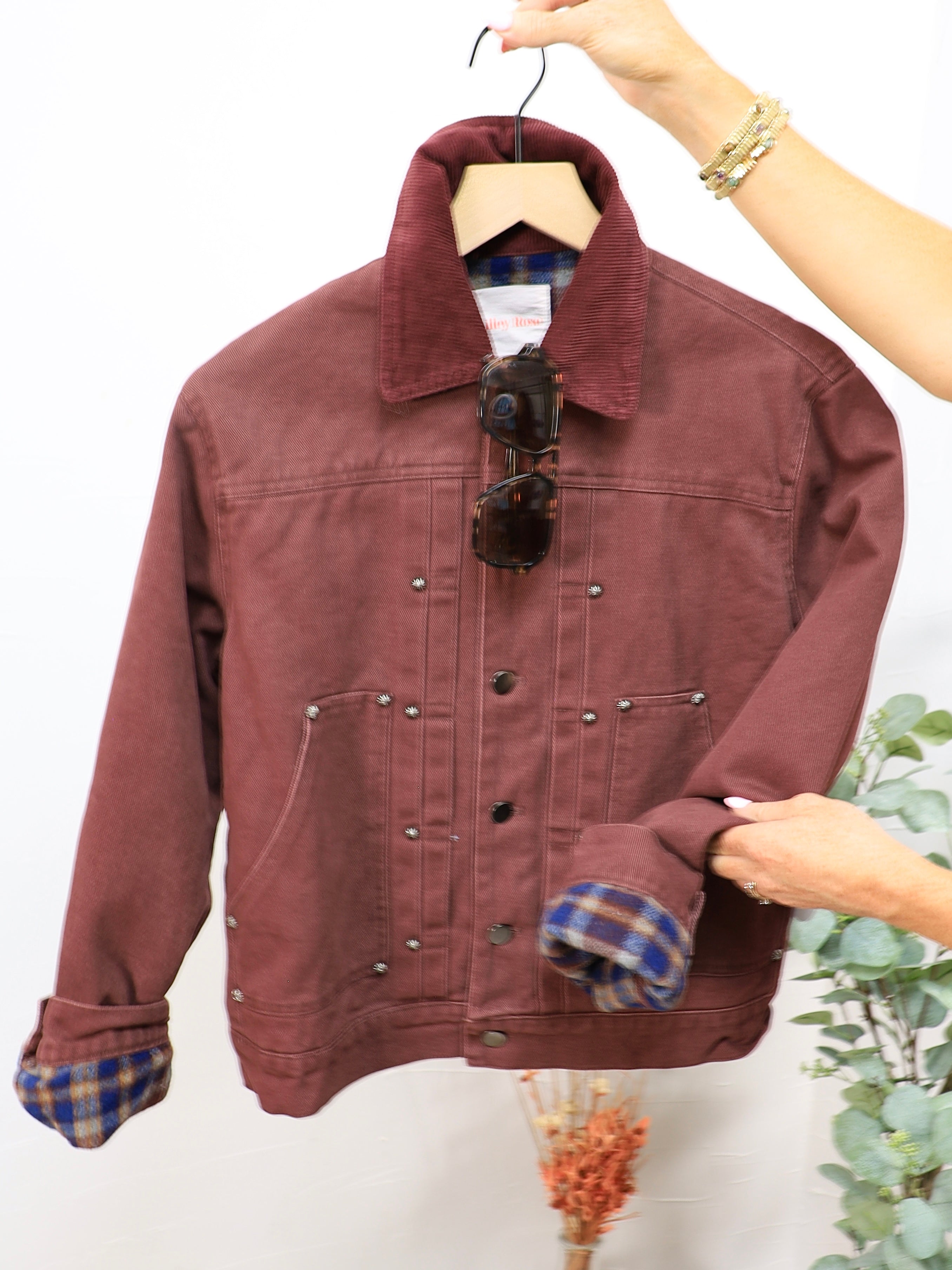 Burgundy twill bomber jacket with plaid flannel lining, corduroy collar, silver snap buttons, displayed on hanger with sungla
