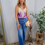 Purple satin cami with cream lace bib detail, styled with high-waisted wide-leg jeans and layered necklaces.