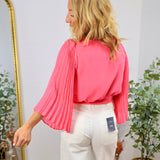 Coral pink wrap blouse with pleated flutter sleeves, styled with white wide-leg jeans, back view.