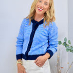 Blue and white ribbed knit cardigan with navy trim and buttons, styled with white trousers.