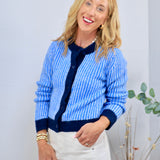 Blue and white ribbed knit cardigan with navy trim and buttons, styled with white trousers.