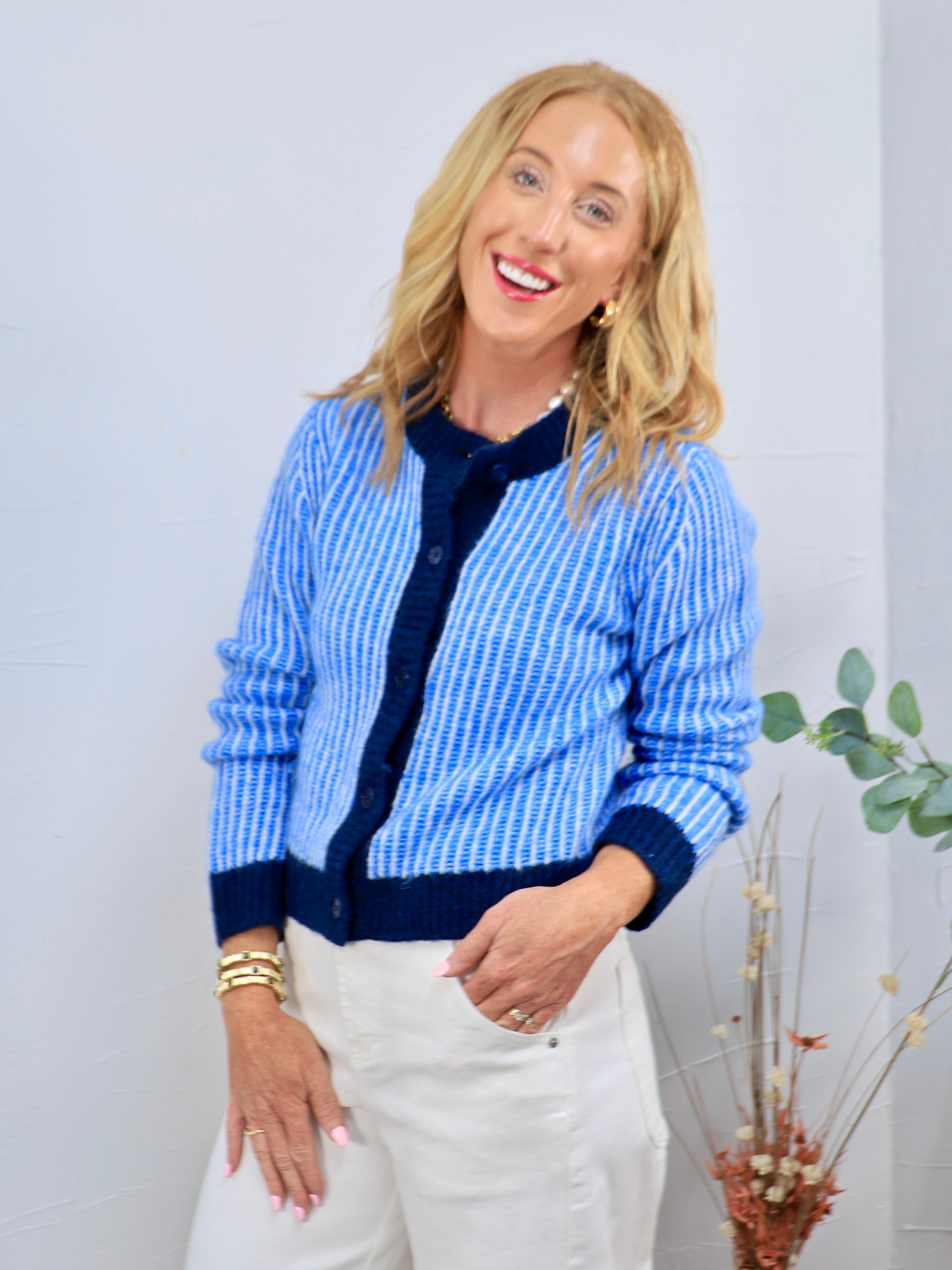 Blue and white ribbed knit cardigan with navy trim and buttons, styled with white trousers.