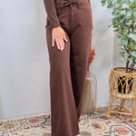 Woman wearing chocolate brown wide leg drawstring denim pants with matching long-sleeve top and tan boots