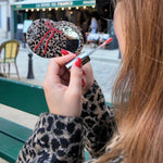 Woman holding a leopard print compact mirror with red bow and lip gloss in Paris