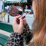 Woman holding a leopard print compact mirror with red bow and lip gloss in Paris