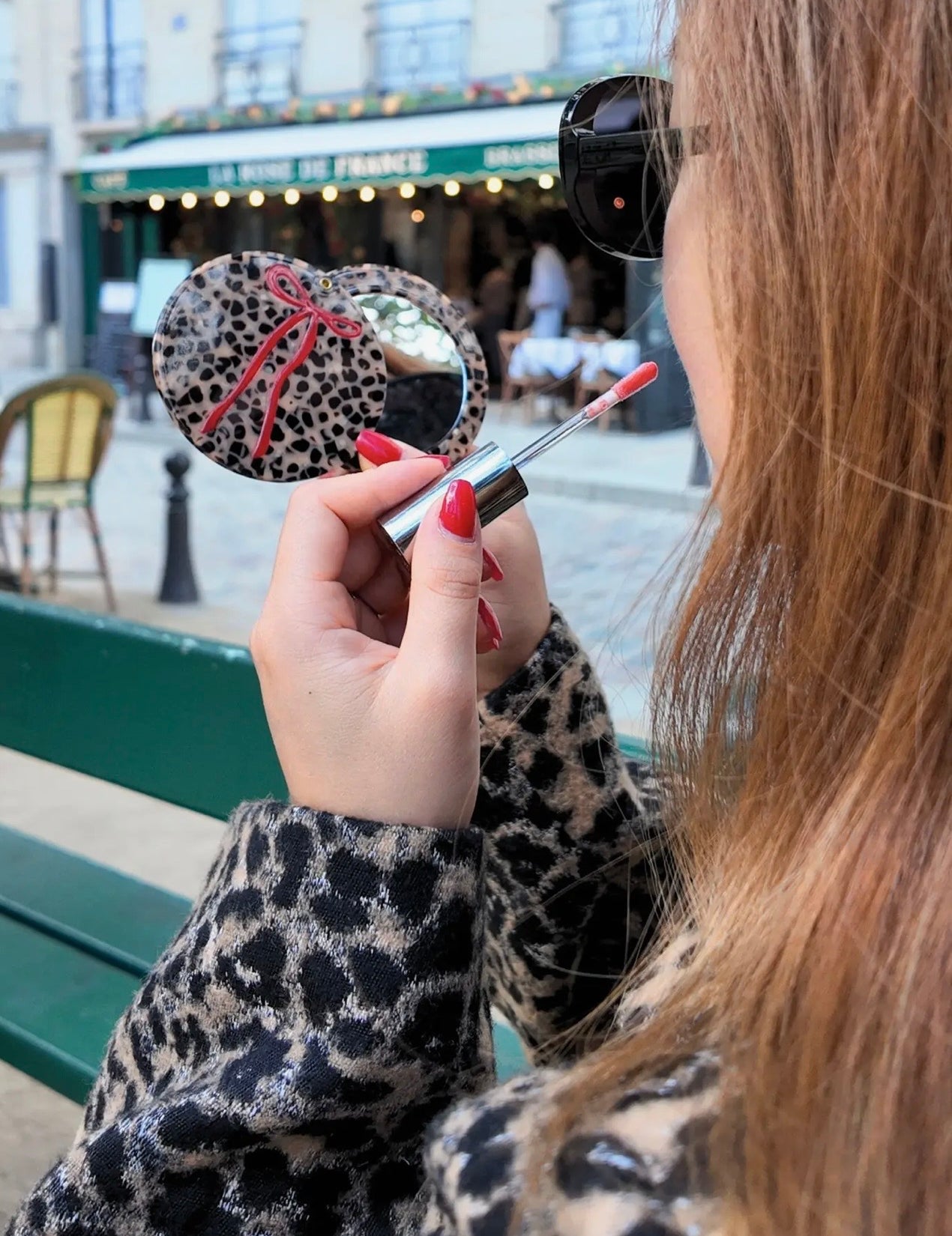 Woman holding a leopard print compact mirror with red bow and lip gloss in Paris