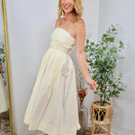 Cream strapless midi dress with ruched bodice and full skirt, styled with espadrille wedge sandals.