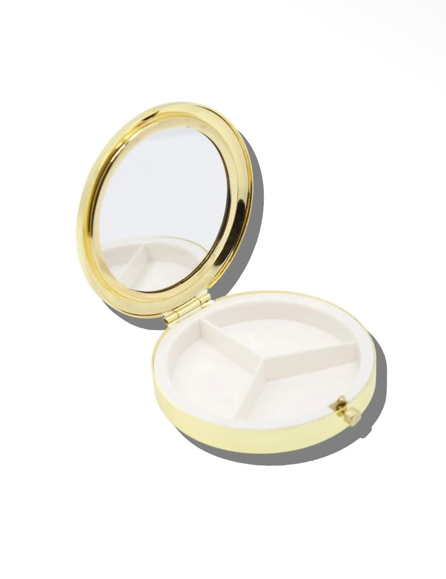 Round yellow and gold pill compact open, showing mirror lid and three-compartment white interior tray.