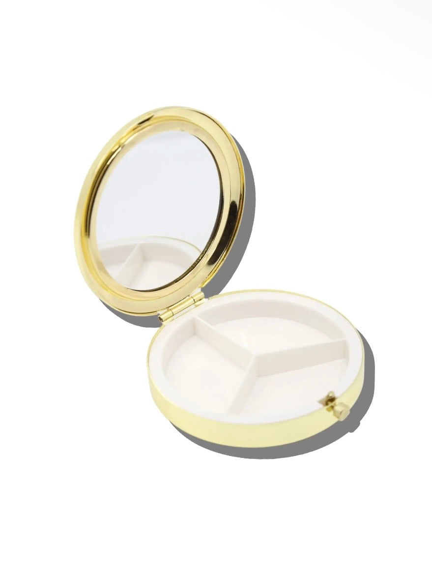Round yellow and gold pill compact open, showing mirror lid and three-compartment white interior tray.