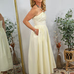Woman wearing yellow halter maxi dress with beaded neckline detail, standing beside gold mirror in boho-styled room.