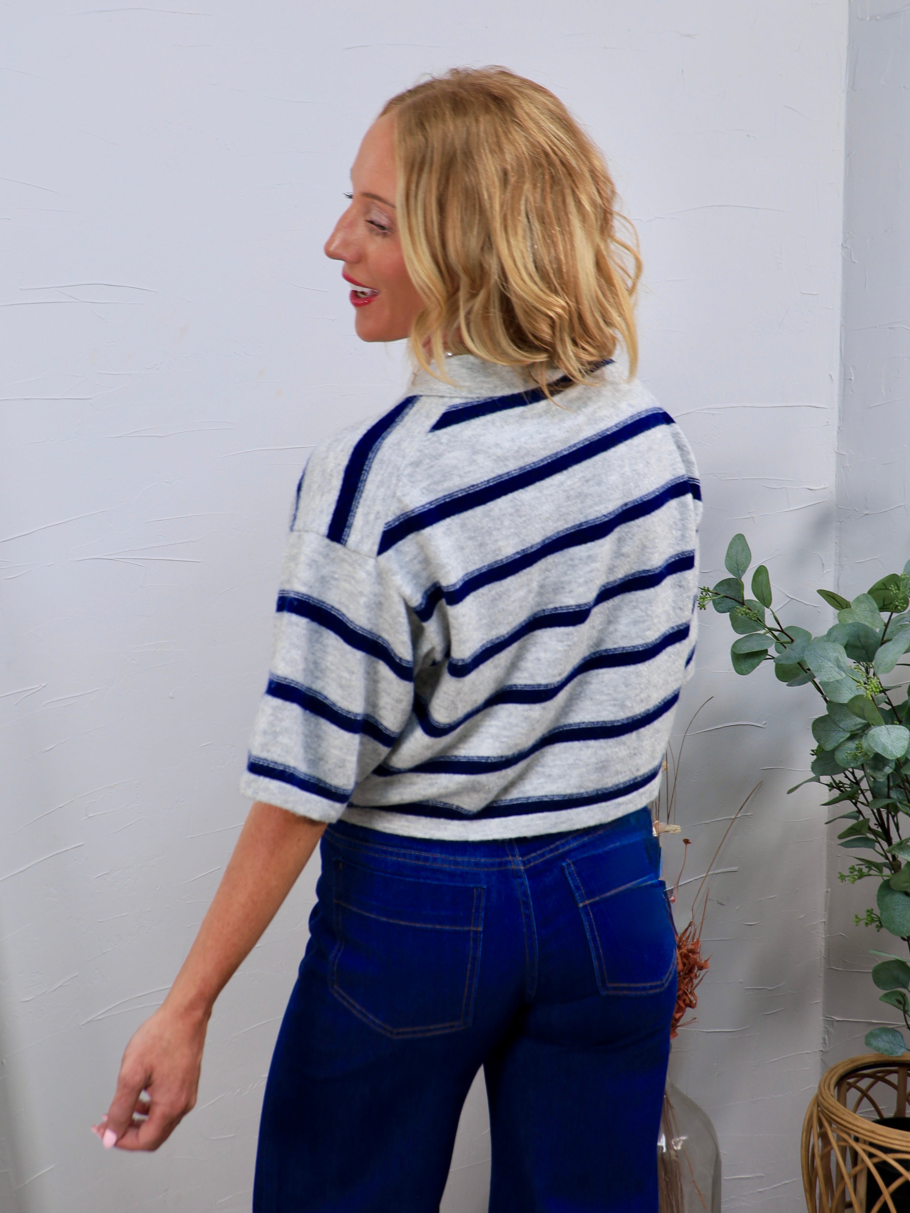 Woman wearing Roy's Rugby Top in gray with navy blue stripes, paired with dark blue high-waisted jeans, back view.