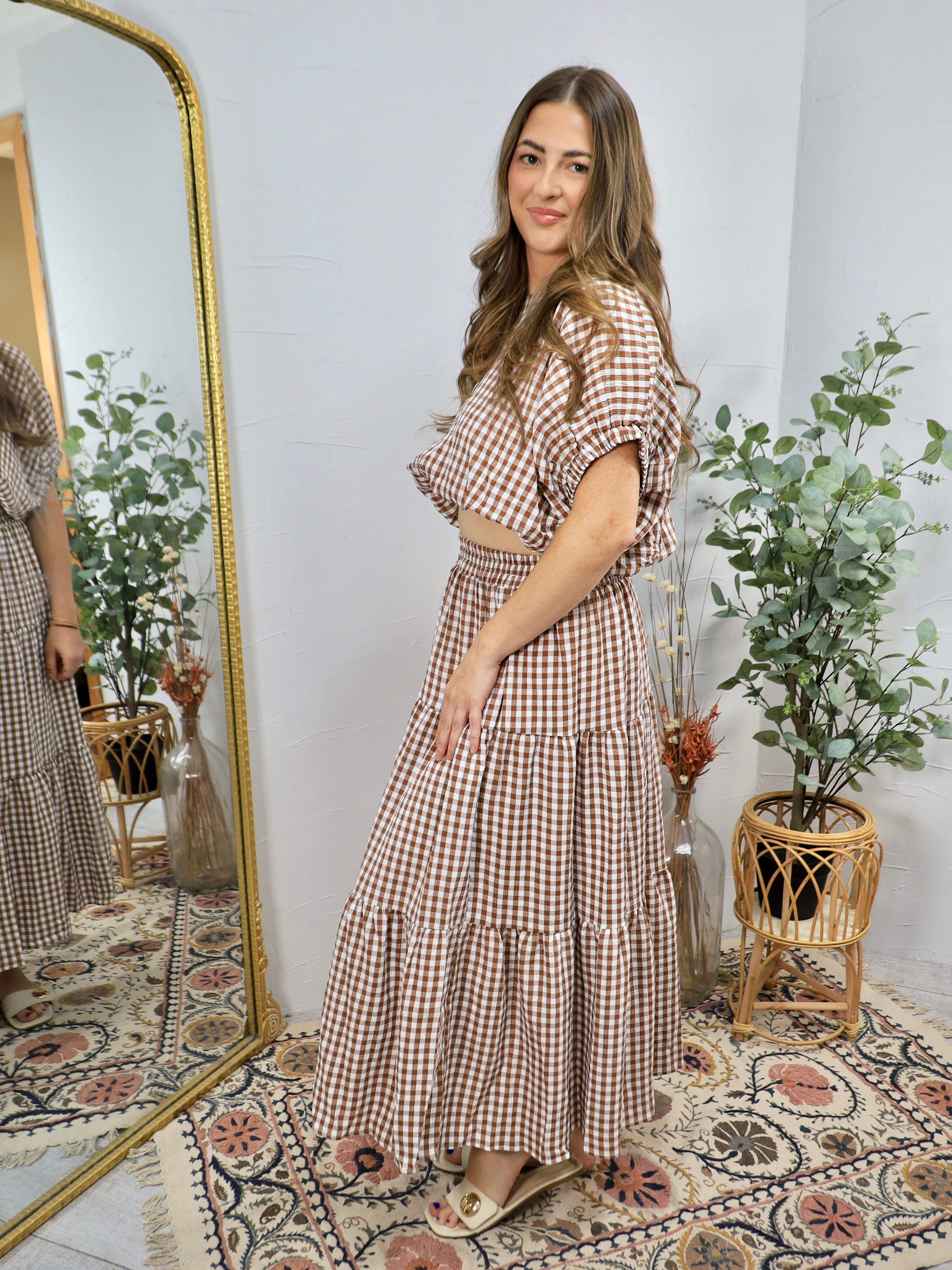 Woman wearing brown and white gingham checkered tiered maxi dress with short sleeves, styled with neutral sandals in boho int