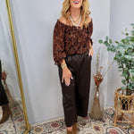 Dark chocolate brown faux leather cropped wide-leg pants with elastic waistband, styled with paisley off-shoulder top and tan