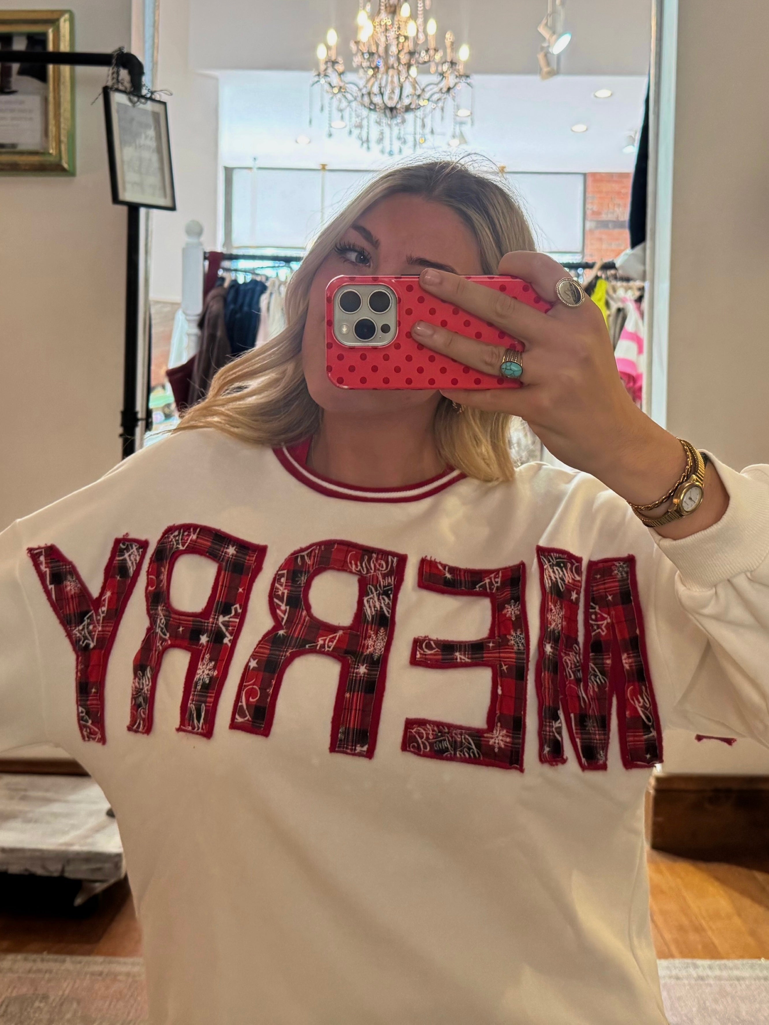 White crewneck sweatshirt with red plaid appliqué "MERRY" lettering, styled with red ribbed neckline trim.