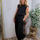 Black sleeveless muscle-tee jumpsuit with drawstring waist, styled with silver sneakers and gold bracelet.