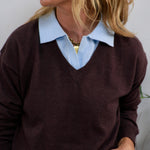 Burgundy v-neck knit sweater layered over a light blue collared shirt, styled with a gold chain necklace.