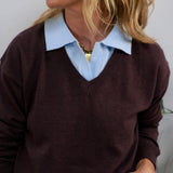 Burgundy v-neck knit sweater layered over a light blue collared shirt, styled with a gold chain necklace.