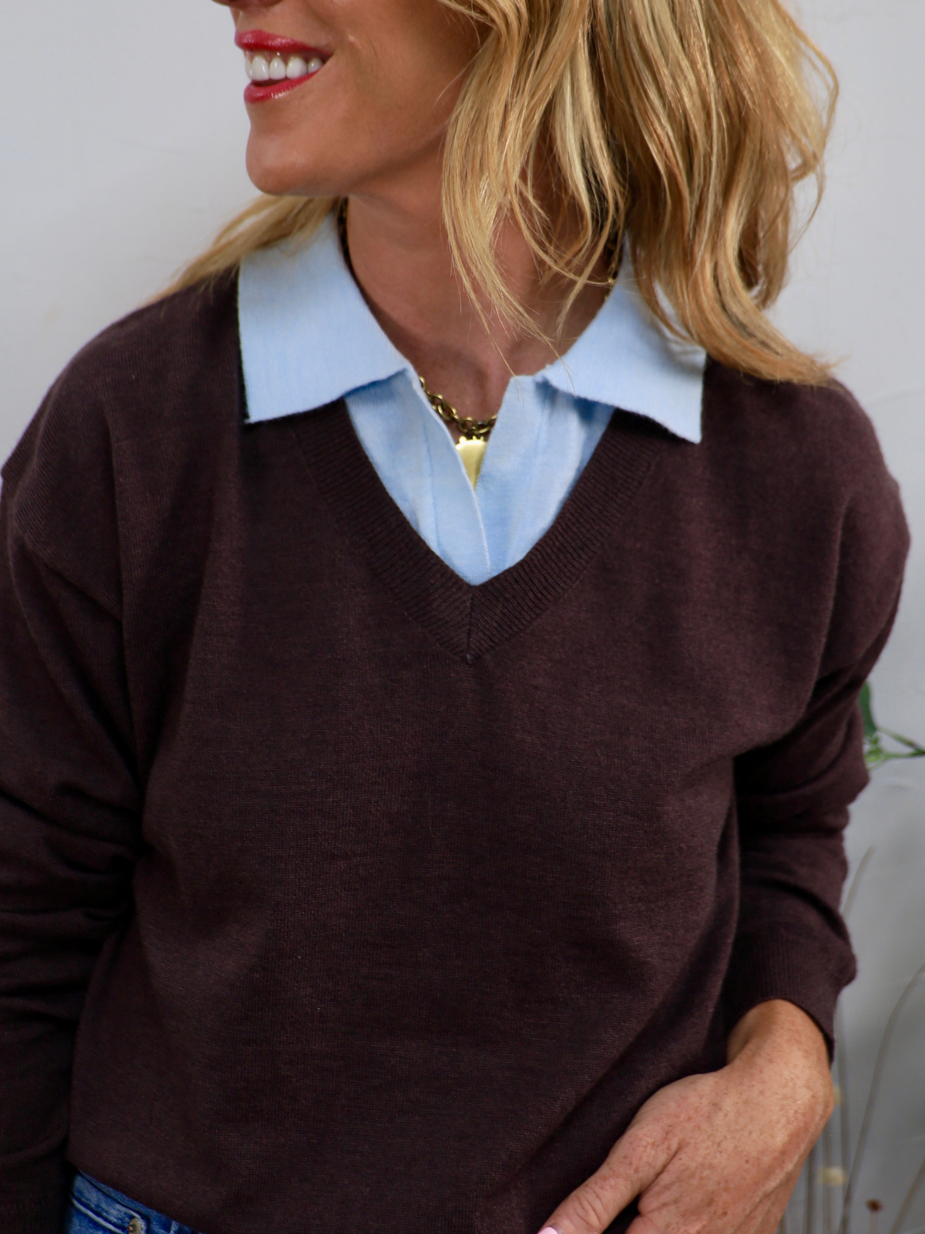 Burgundy v-neck knit sweater layered over a light blue collared shirt, styled with a gold chain necklace.