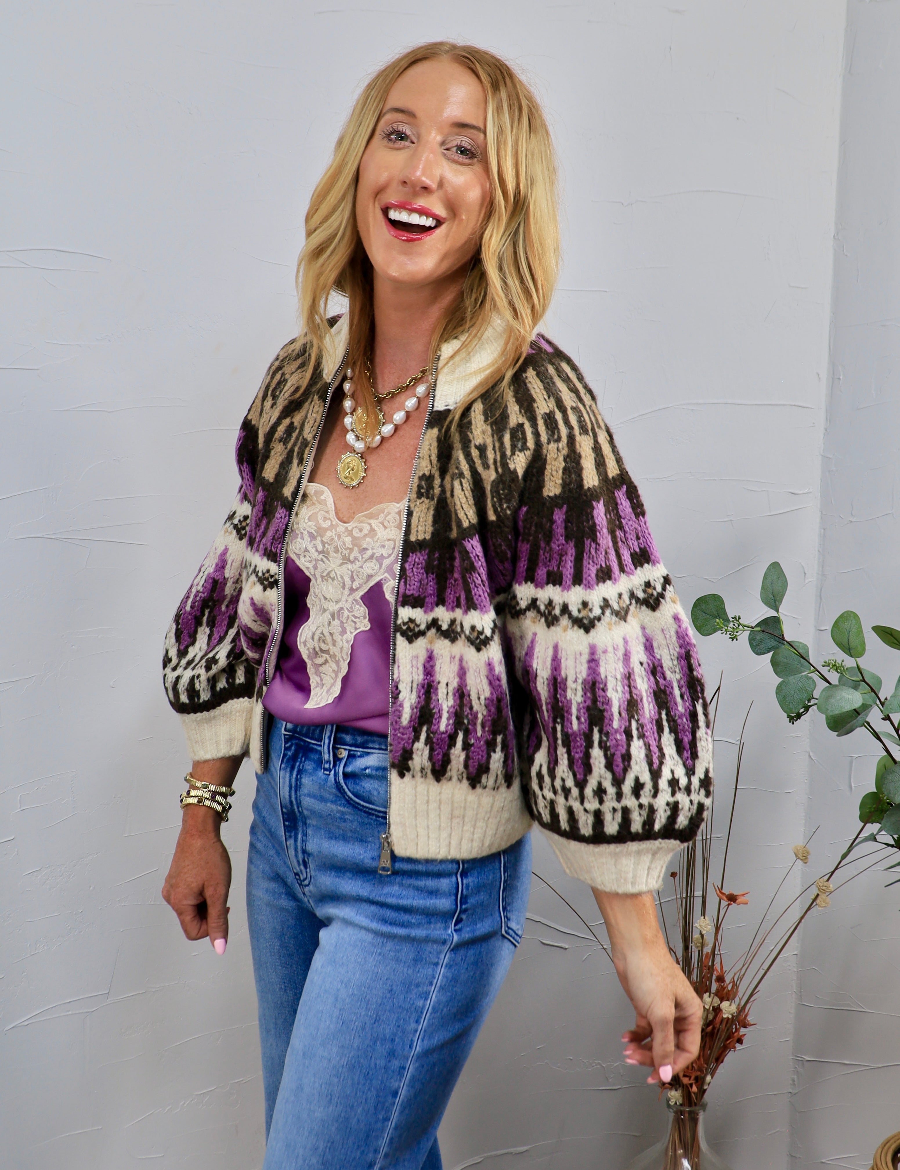 Woman wearing cropped purple and cream Fair Isle zip-up sweater with balloon sleeves and blue jeans