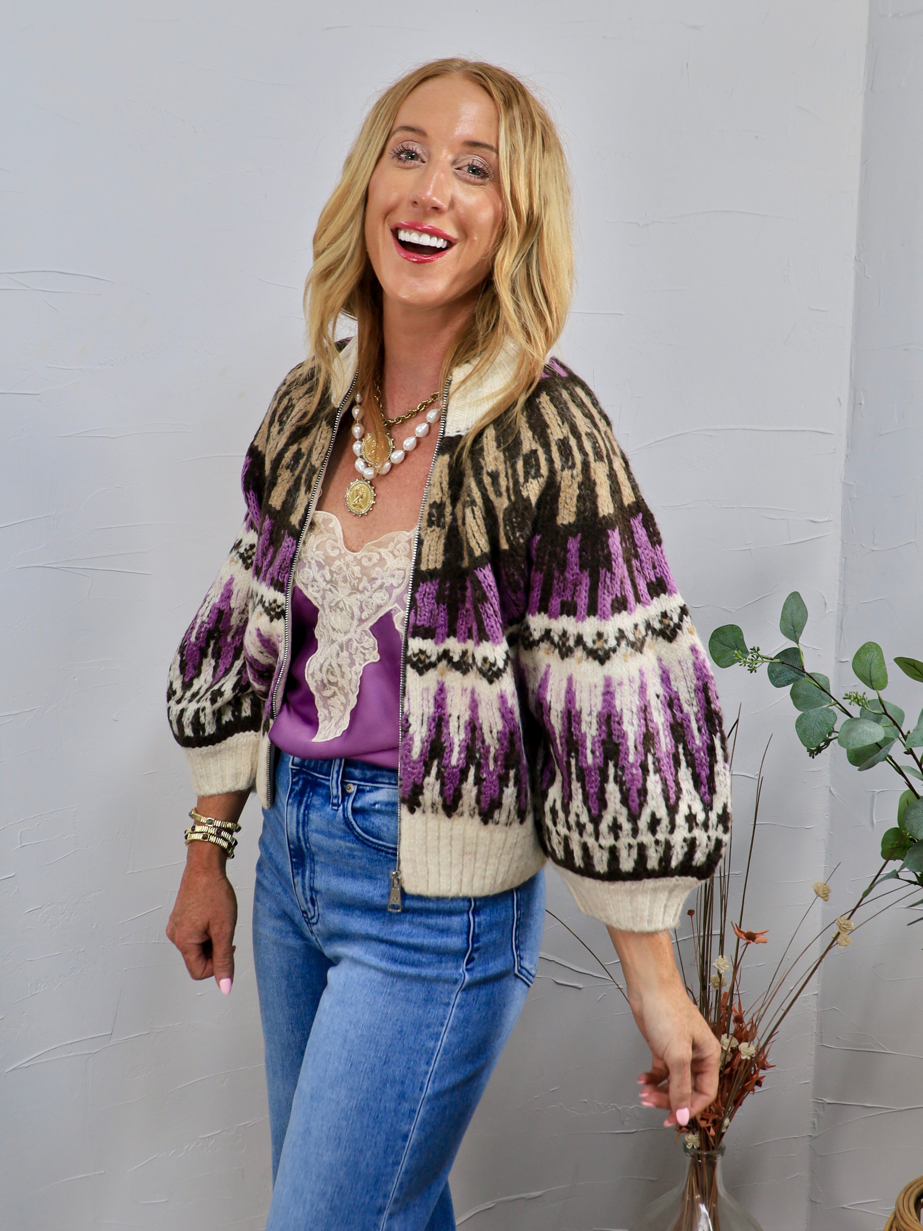 Woman wearing cropped purple and cream Fair Isle zip-up sweater with balloon sleeves and blue jeans