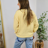 Pale yellow crewneck sweater styled with light wash jeans, shown from the back on a smiling brunette model.