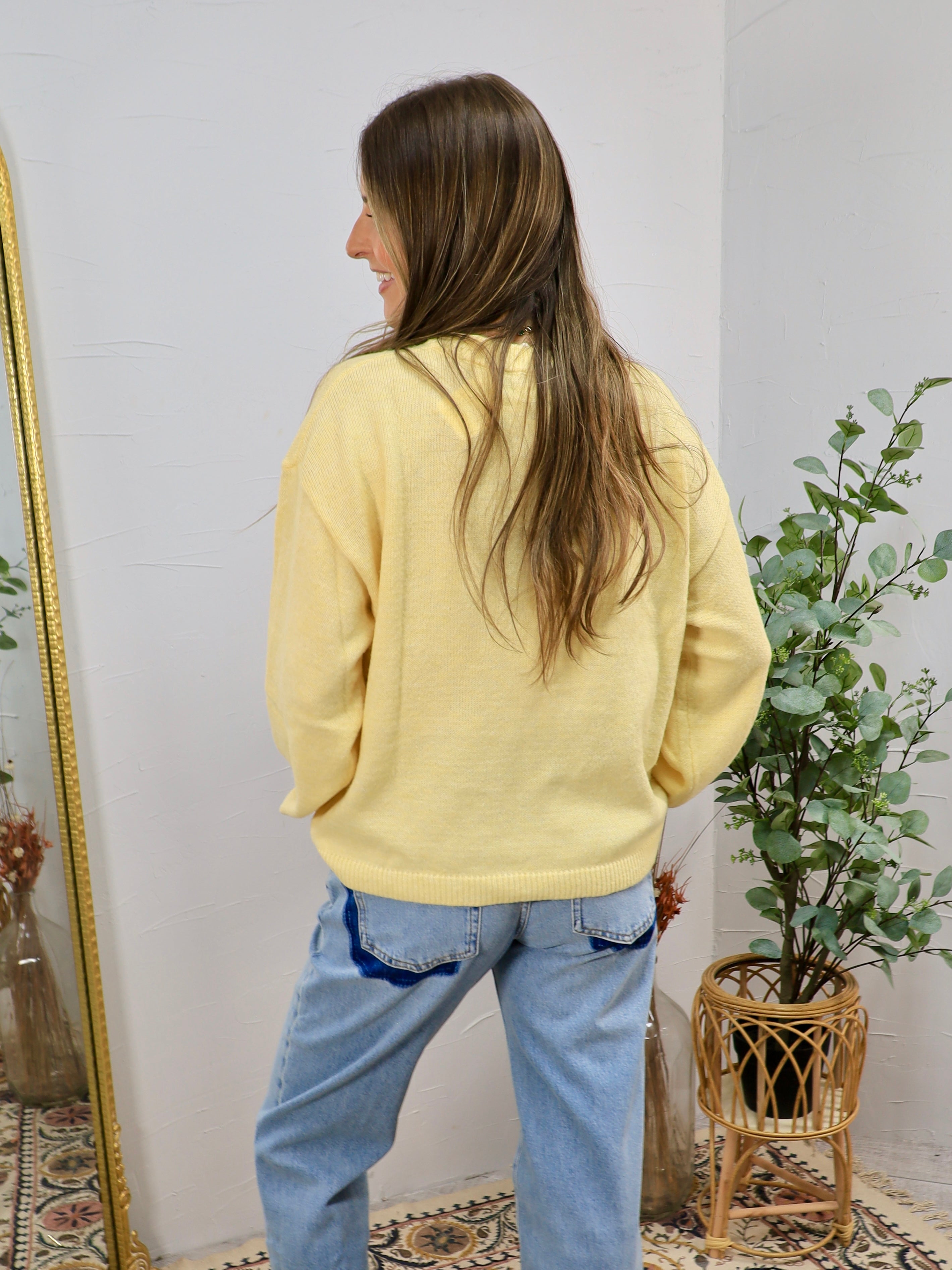 Pale yellow crewneck sweater styled with light wash jeans, shown from the back on a smiling brunette model.