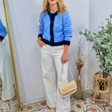 Blue and white striped fitted cardigan with navy trim, styled over navy top with wide-leg white trousers.