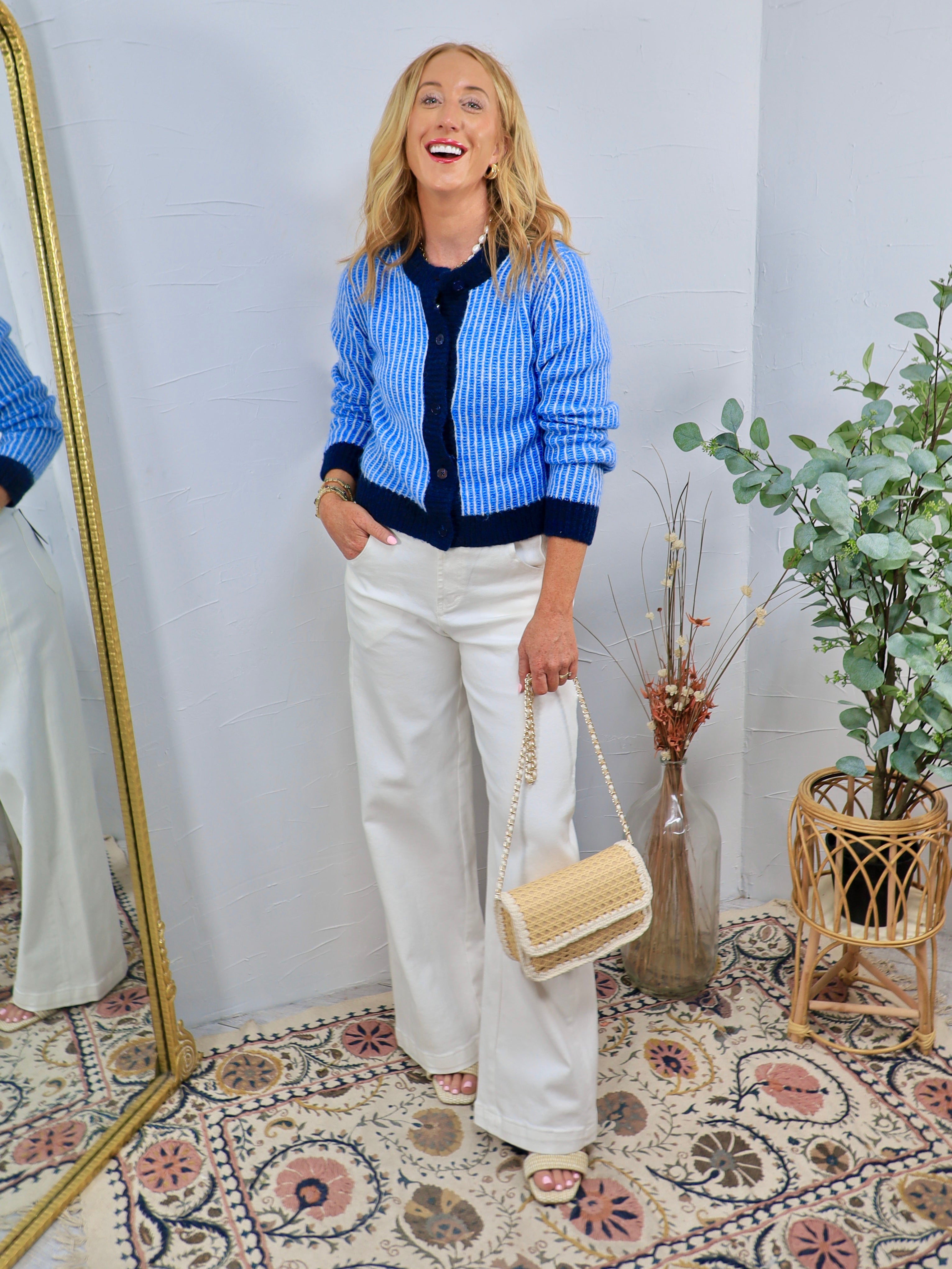 Blue and white striped fitted cardigan with navy trim, styled over navy top with wide-leg white trousers.